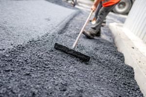 Worker levelling fresh asphalt on a road construction site, indu